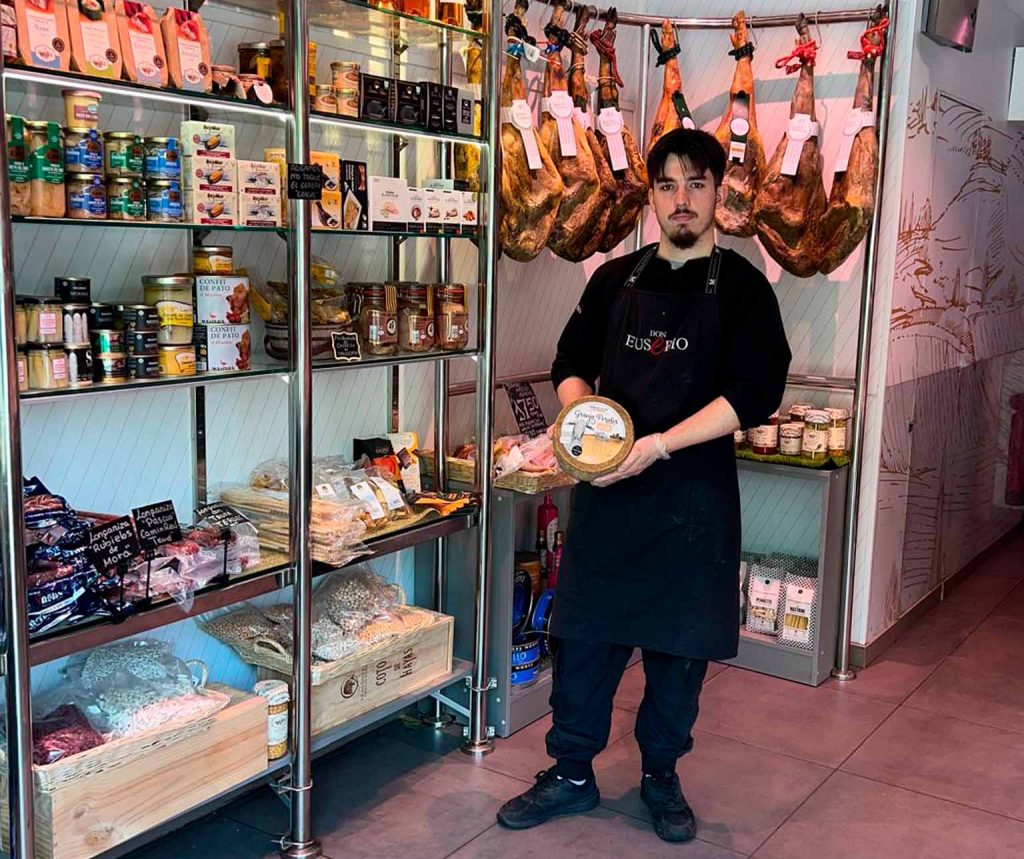Pablo con queso Granja Perales en Charcuterías Pascual Zaragoza Imagen de Pablo en el interior de Charcuterías Pascual, en Miguel Servet 87, Zaragoza, sujetando un queso Granja Perales dentro de la selección de quesos artesanos y productos gourmet de la tienda.
